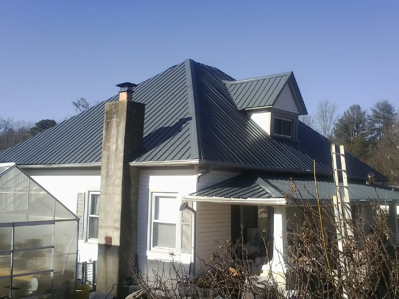Dark blue standing seam metal roof on a white farmhouse with dormer — Slate & Tile Roof Repair by Roofing Brothers in Chapin