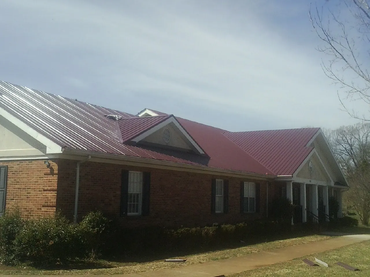 Red metal roof with gabled entries on a long brick building, from a Hail Damage Roof Repair job in Chapin
