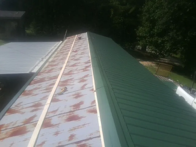 Old rusted panels beside newly installed green metal roofing — Wind Damage Roof Repair by Roofing Brothers in Chapin