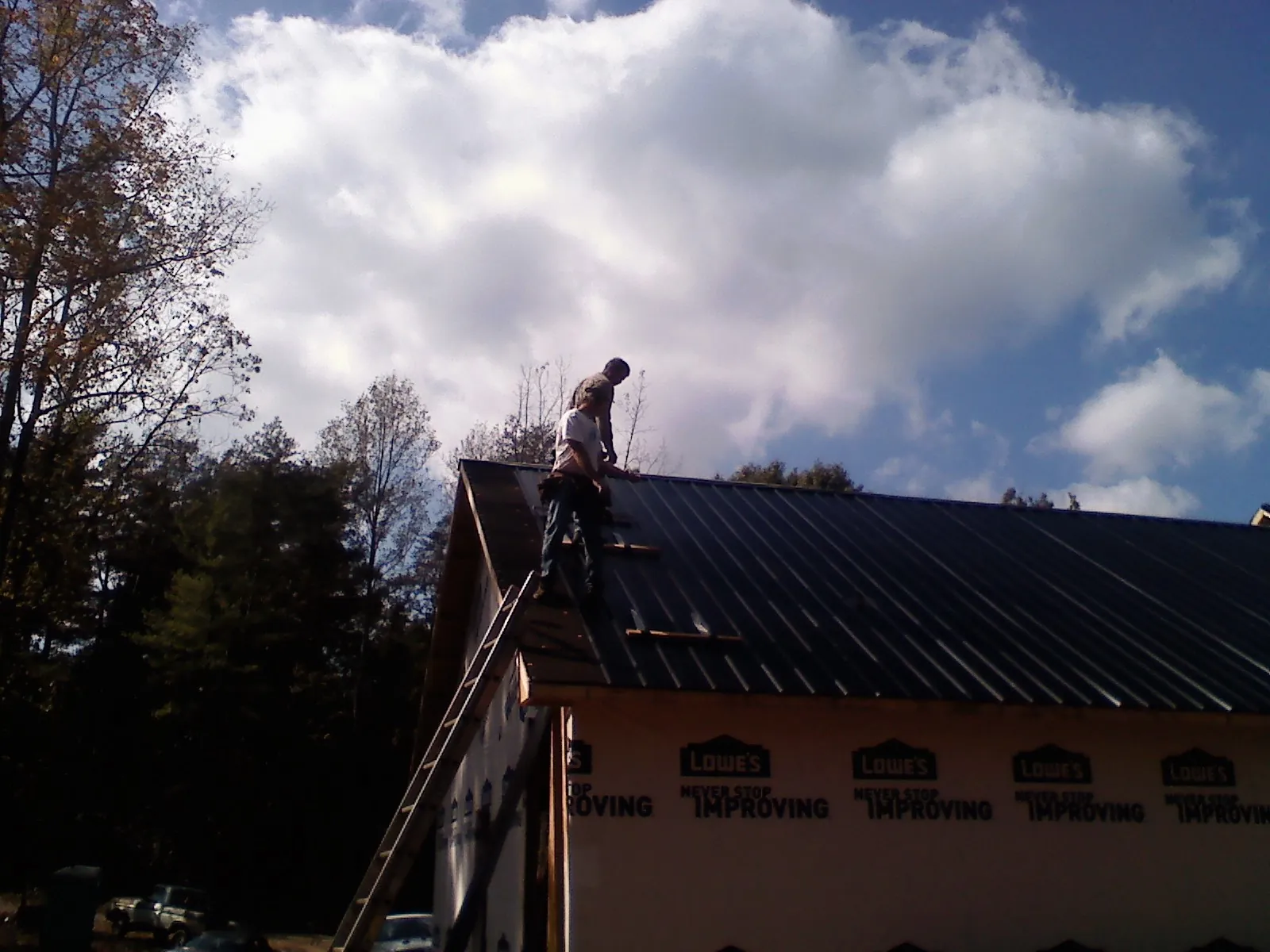 Roofer fastening dark metal panels high against a cloudy sky, from a Roof Inspection job in Chapin