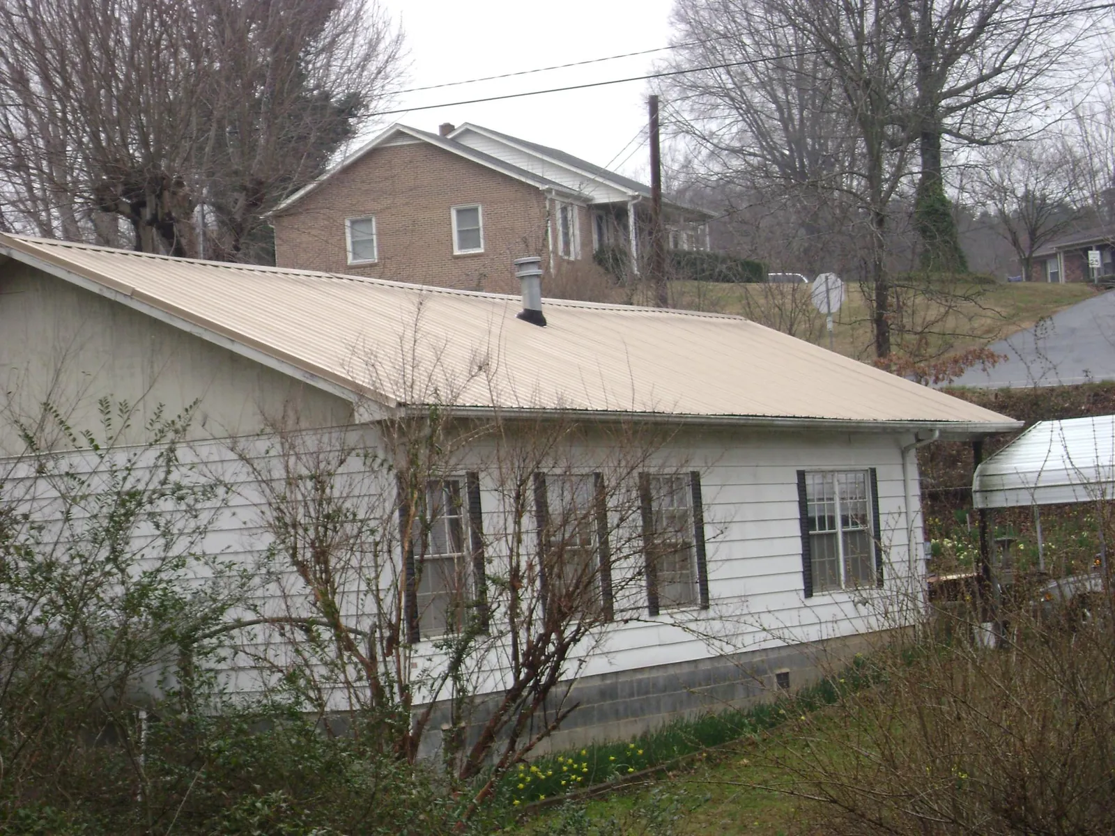 Tan metal roof on a white sided house set into a hillside — Commercial Roofing by Roofing Brothers in Chapin